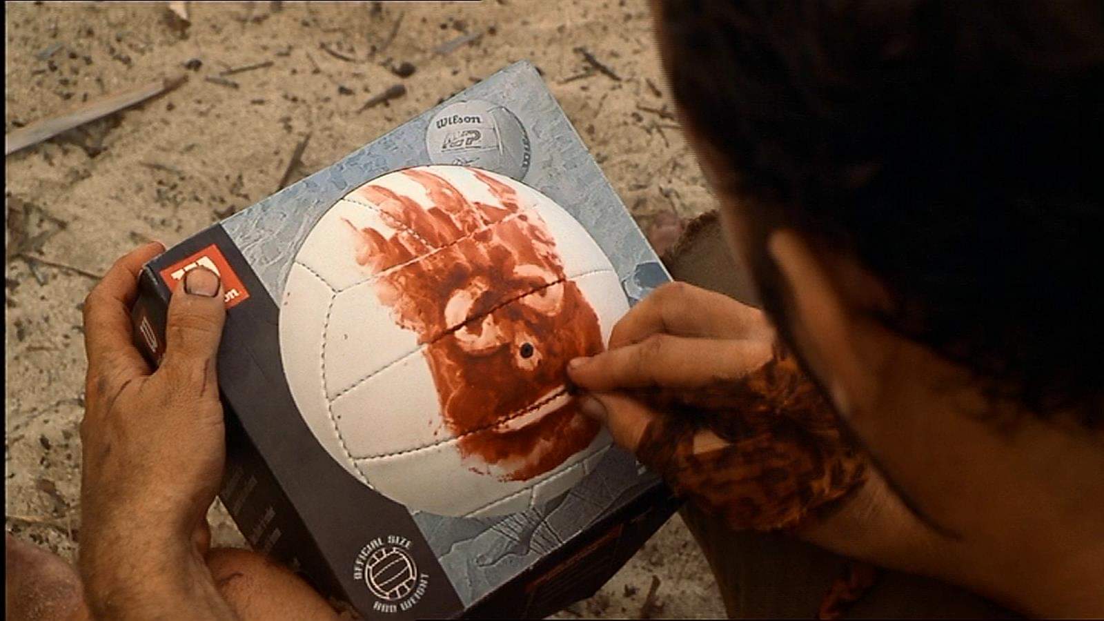 Tom Hanks draws a face onto a white football using his blood