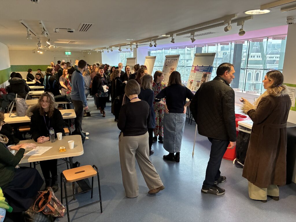 Conference attendees mingle in a bright meeting space with a mix of tables and chairs and standing room