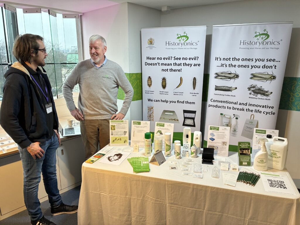A staff member from Historyonics stands by a display of their pest control products, talking to a conference attendee