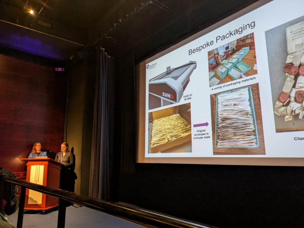Joanne and Isabelle stand at the lectern in Cubby Broccoli, to the side of the cinema screen showing their slides on bespoke packaging