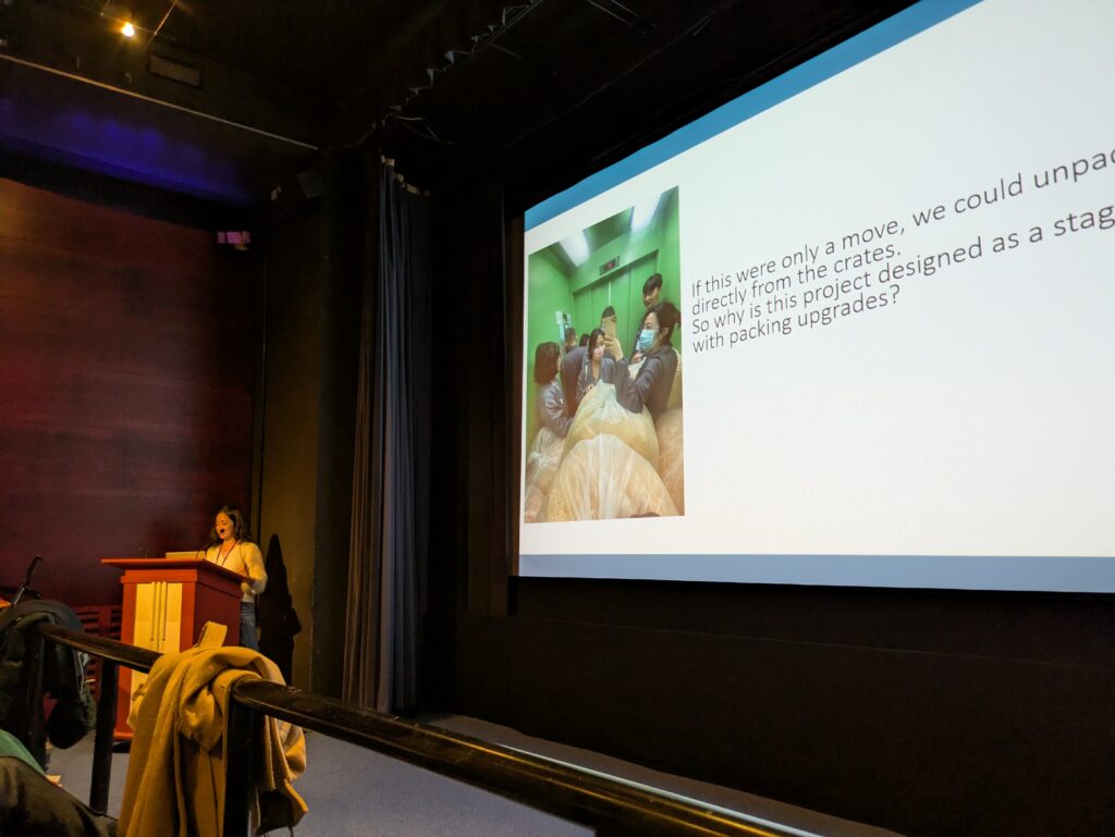 Yu-Hsin gives her presentation, with a slide showing an image of staff squeezed into a lift alongside packing materials