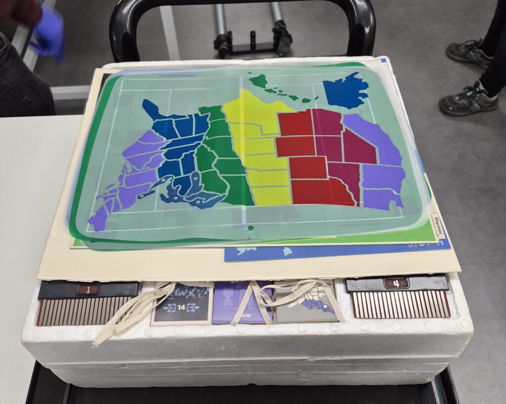 Colourful plastic screen overlays laid on top of a white box containing the console and game cartridges.