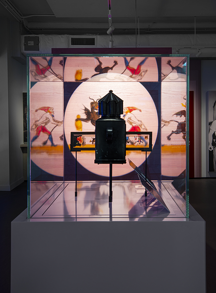 A brightly projected illustrated slide, seen through a glass case containing a historic projector