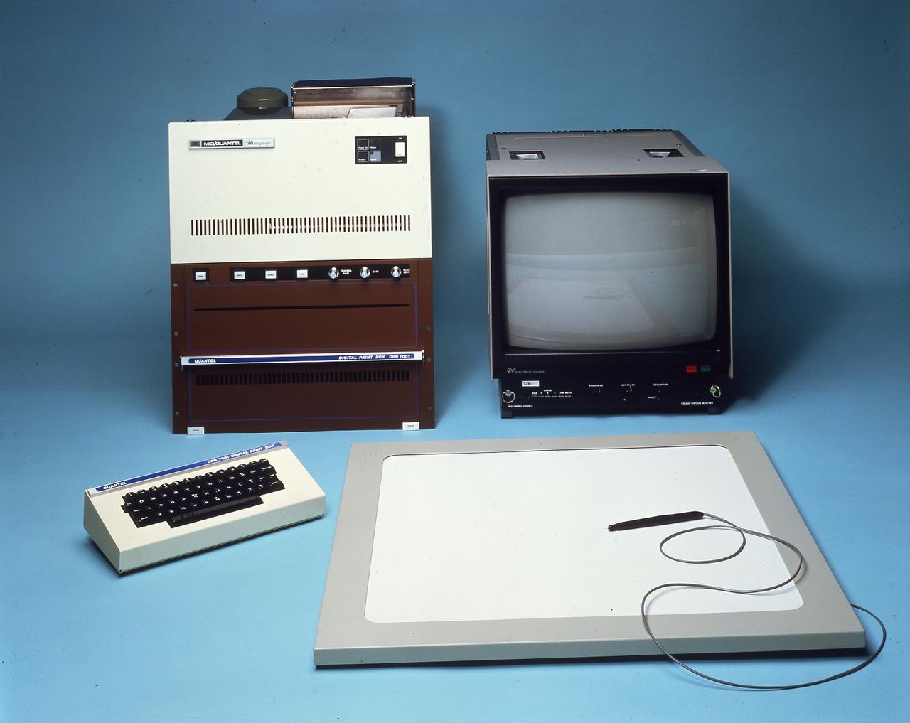 An early graphics tablet with stylus, small keyboard, display monitor and processing unit, against a blue background