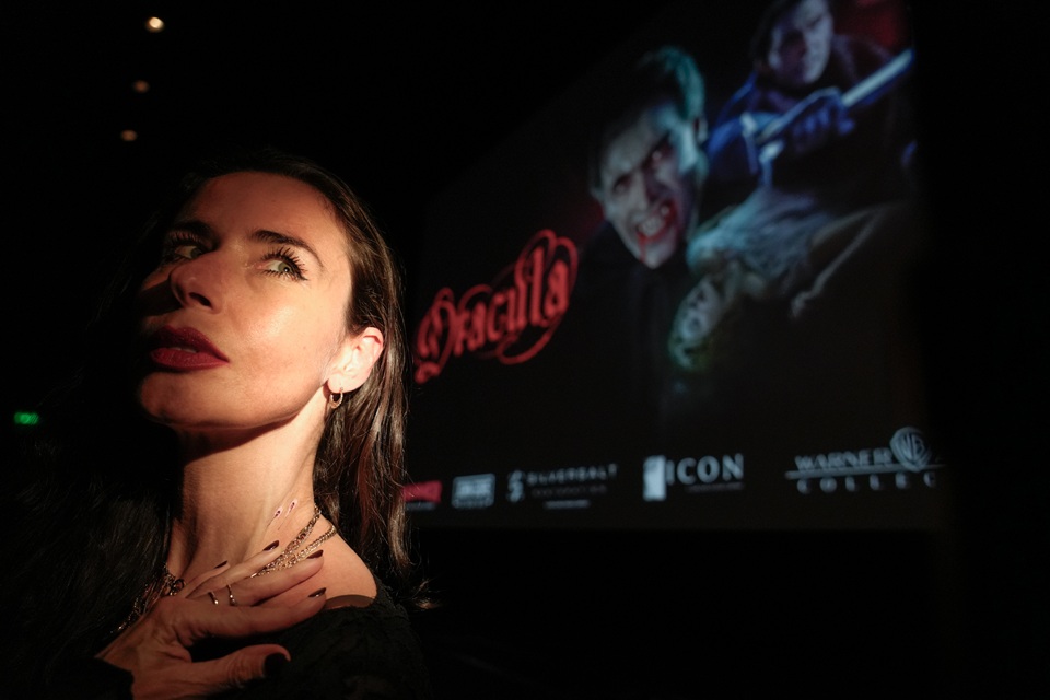 A woman with imitation vampire bite marks on her neck looks over her shoulder; behind her the poster for Hammer's Dracula is on the cinema screen