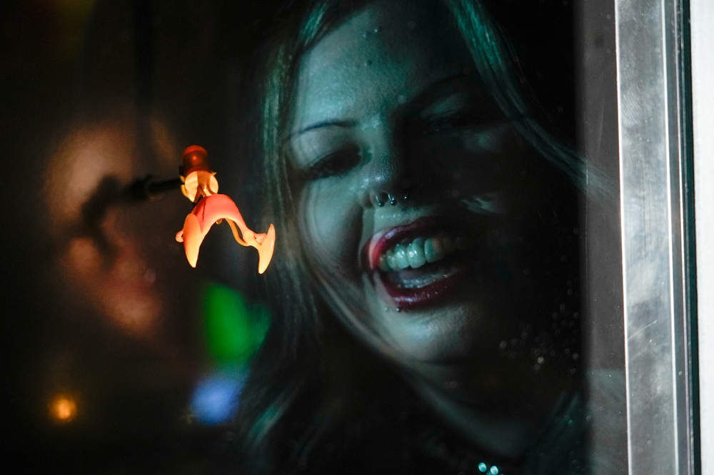 A woman's blurry face can be seen looking into a glass case containing Christopher Lee's dracula fangs