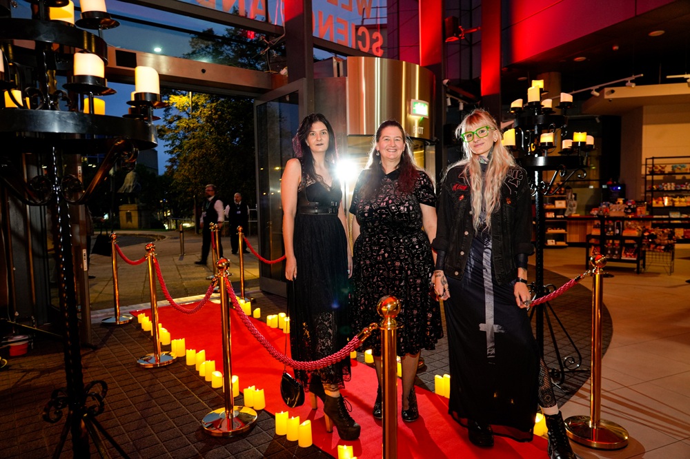 A group of three women in black dresses pose for a photo, smiling