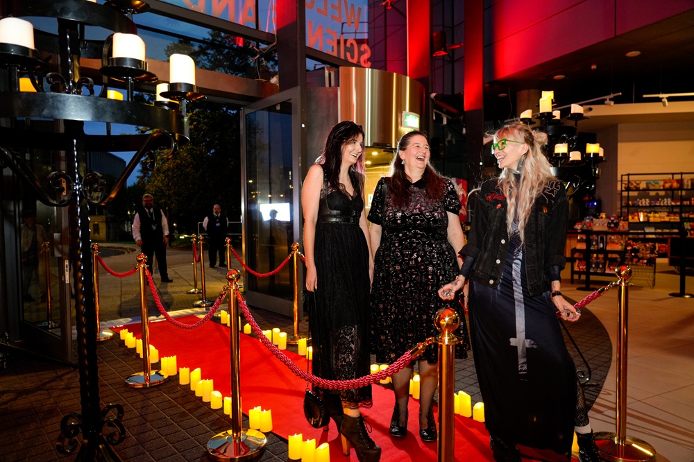 A group of three women in black dresses pose for a photo, looking at each other and laughing