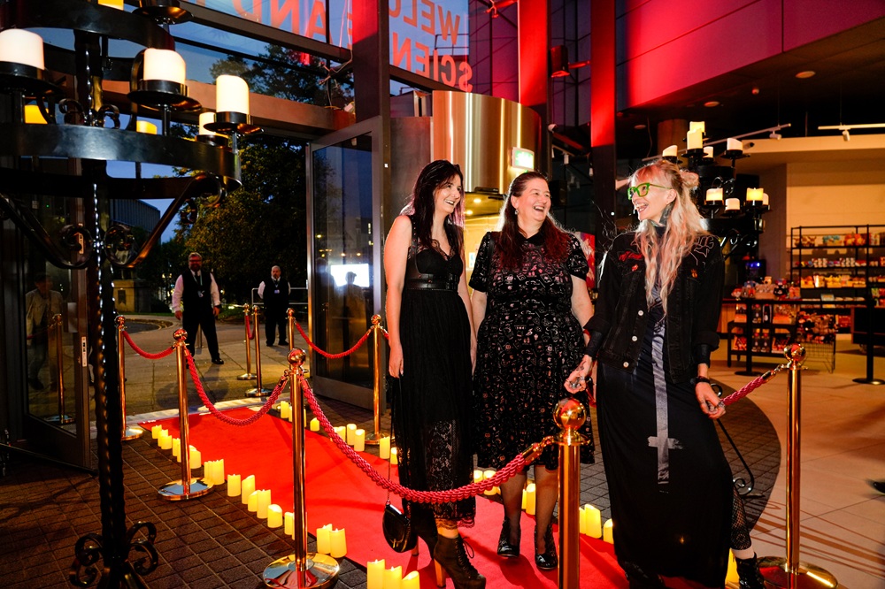 A group of three women in black dresses pose for a photo, looking at each other and laughing