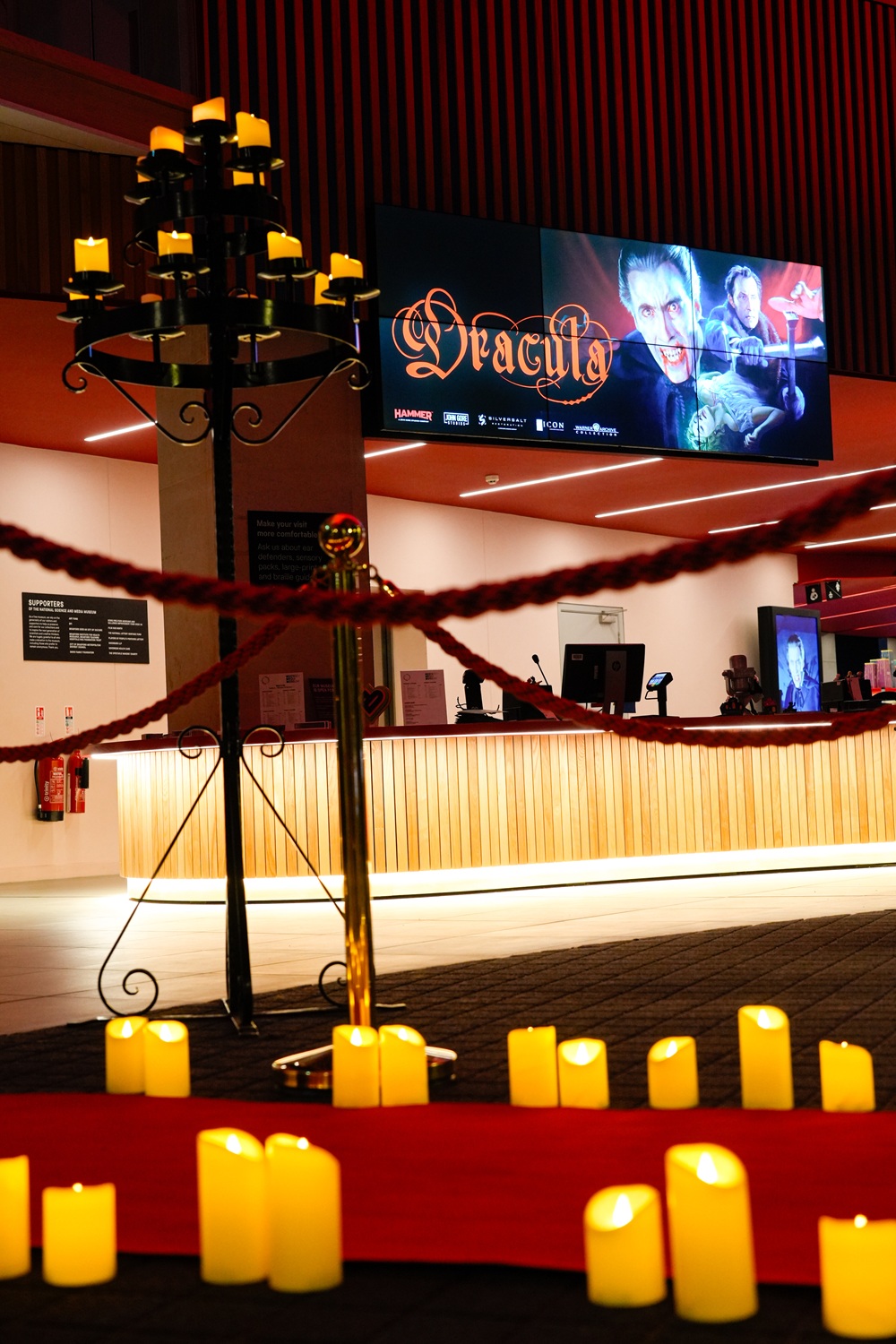 The foyer dressed with candles and red ropes along the red carpet; a large image of Dracula is on the digital screens above the welcome desk