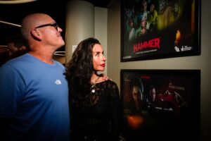 A man and woman stand together and look at the Hammer posters on the wall of Pictureville bar.