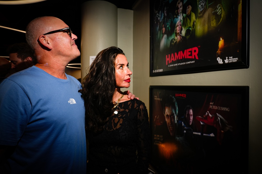 A man and woman stand together and look at the Hammer posters on the wall of Pictureville bar.